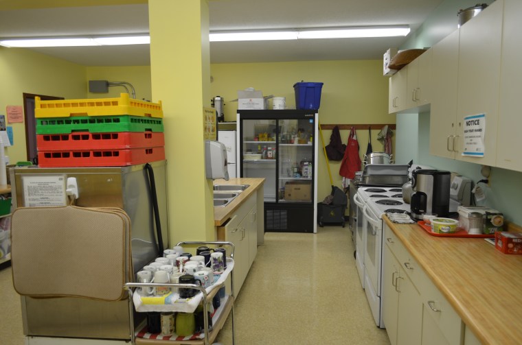 Photo of kitchen showing industrial fridge, two stoves and ovens, three sinks and industrial dishwasher.
