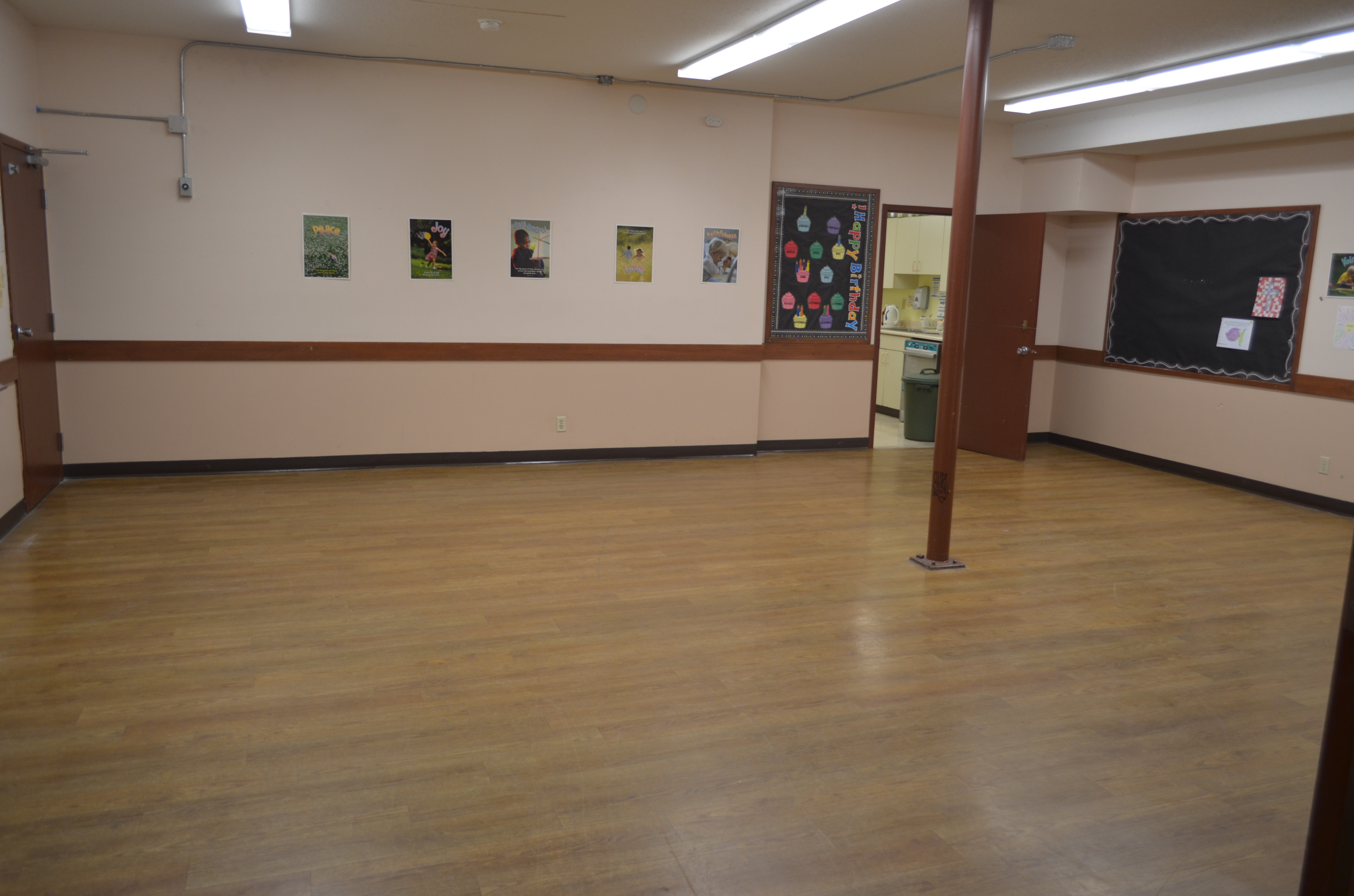 Image shows the Mark Meeting Room which has laminate flooring and is located next to the kitchen. There is a metal support pole in the middle of the room.